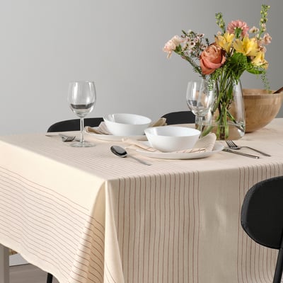 Elegante tavola apparecchiata con tovaglia a righe, ciotole bianche, posate, bicchieri da vino e centrotavola floreale.
