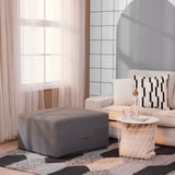 Divano beige con cuscini a righe, pouf grigio, tappeto fantasia, tavolino con oggetti.