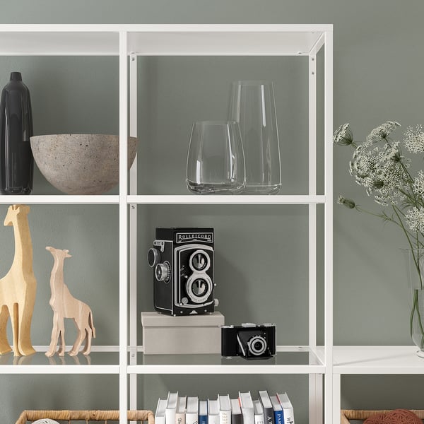 Libreria con ripiani in vetro che contengono oggetti decorativi, macchina fotografica, libri e figure di giraffe contro una parete verde.