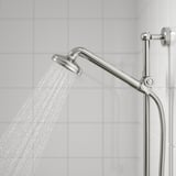 Una combinazione di soffione cromato e cornetta su un binario. Il soffione spruzza acqua in modalità a spruzzo completo.