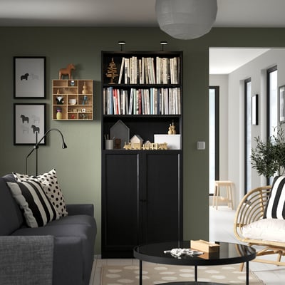 Modern living room with grey sofa, black BILLY bookcase filled with books, decorative items, and prints on olive green wall.