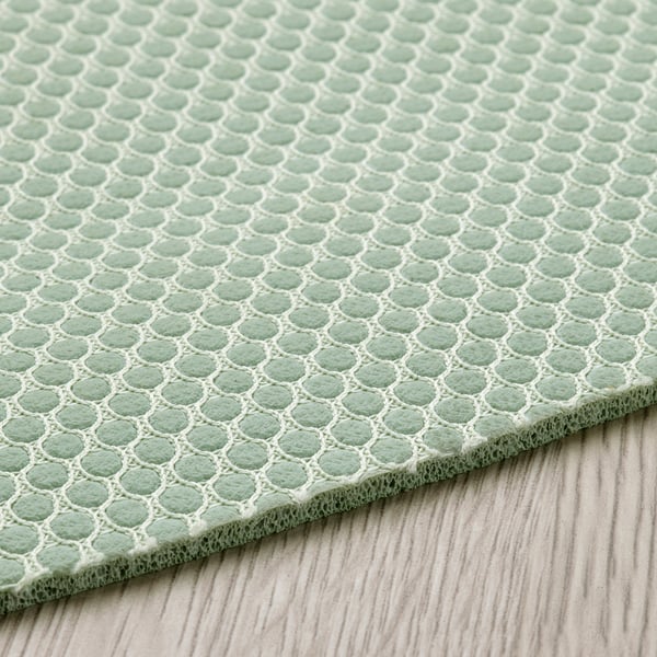 A green exercise mat with a mesh pattern, laid out on a wooden floor. It appears soft and durable, designed for comfort during workouts.