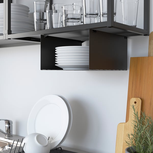 Black kitchen shelf holding clear glasses and white plates. Below, a drainer with a white plate and cup. To the right, a wooden chopping board.