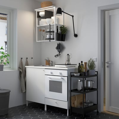 Modern kitchen setup with white ENHET units, narrow black-tiled floor, integrated appliances, open shelving, and wall-mounted light.