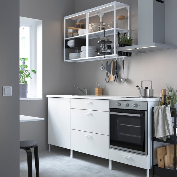 Modern white ENHET kitchen with integrated oven, sleek cabinetry, and open shelves, surrounded by grey walls and a window.