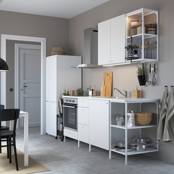 Modern white IKEA ENHET kitchen with oven, sink, open storage.
