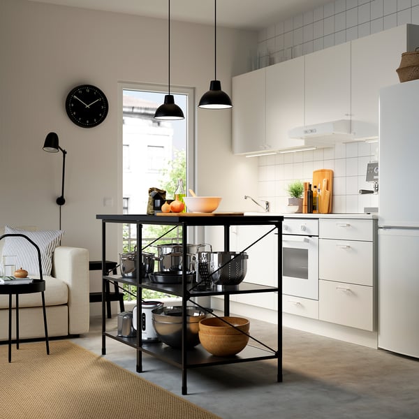 Modern kitchen with white cabinets, black accents, stainless steel appliances, and a central island. Hanging lights and a wall clock.
