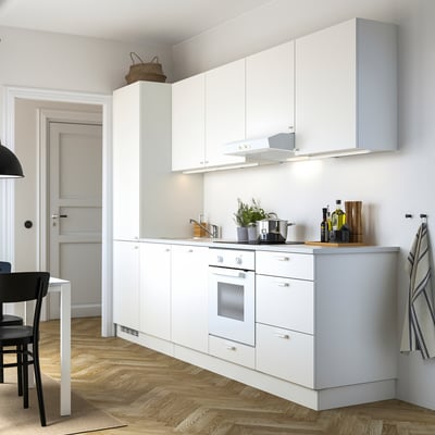 Small modern kitchen with white cabinets, wooden table, black chairs.