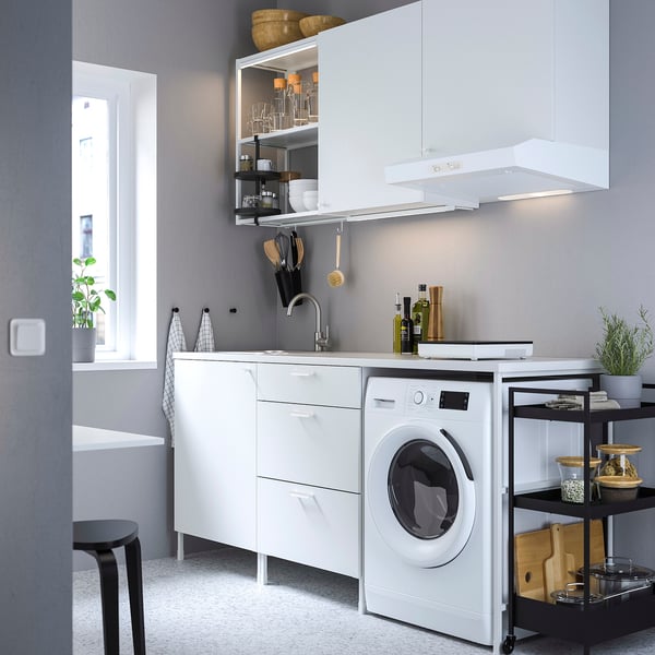Modern compact white kitchen with cabinets, washing machine, and sink. Includes shelves, utensils, and appliances. Clean and minimalist design.