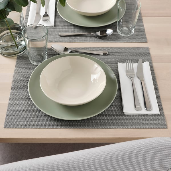 Two place settings with green-rimmed plates, bowls, glasses, and utensils on woven placemats.