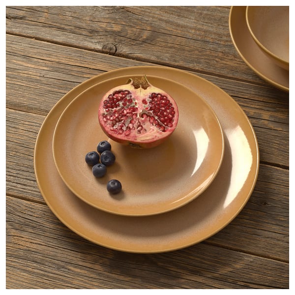 Rustic tan ceramic plates stacked with half pomegranate and blueberries on weathered wood.