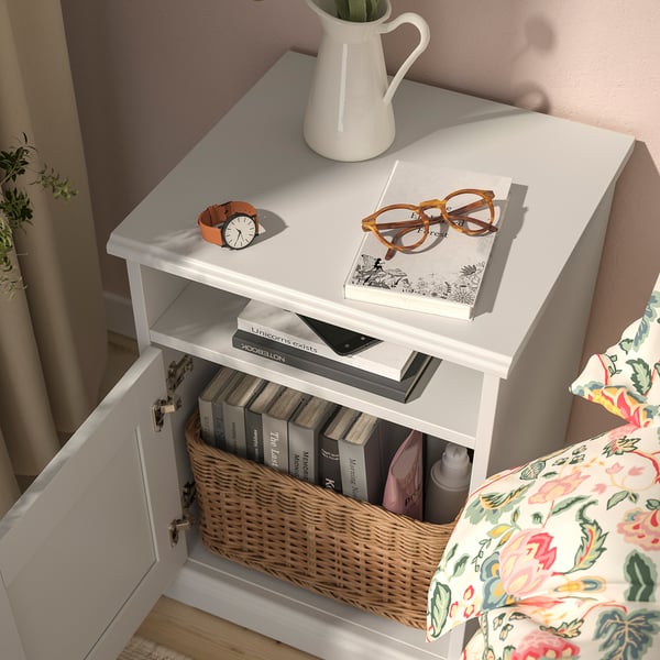 White bedside table with a book, glasses, and a clock. Bottom shelf holds books and a basket.