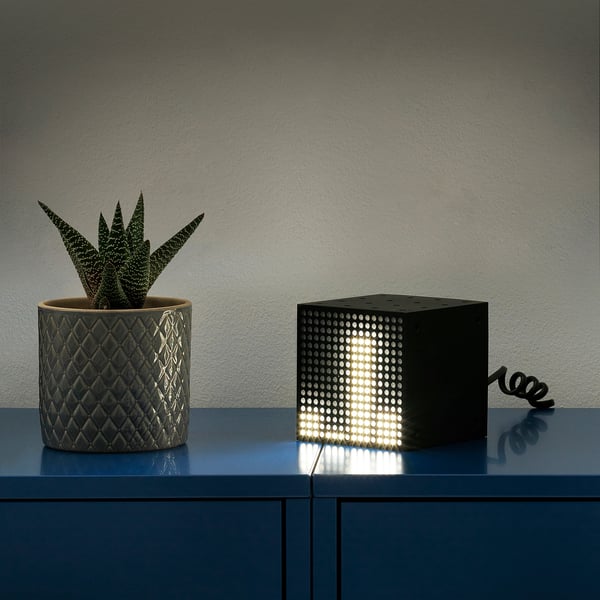 A small cube lamp named FREKVENS sits beside a potted succulent. It responds to sound with light patterns connected by a cord.