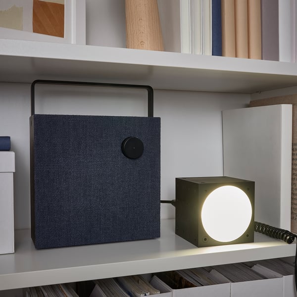 On a shelf, a FREKVENS speaker with a 3-way spotlight: fixed, pulsating, or music-sync modes. The spotlight is dimmable and controlled from the back.