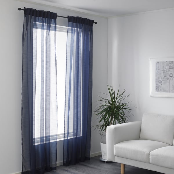 Living room corner with window, sheer blue-gray curtains, white armchair, and plant.