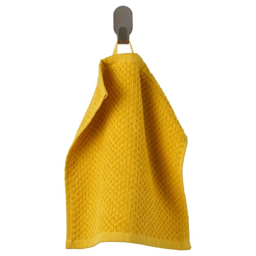 Bright yellow GULVIAL towel hanging on a wooden hook, made of soft 100% cotton, featuring a textured pattern and folded design.