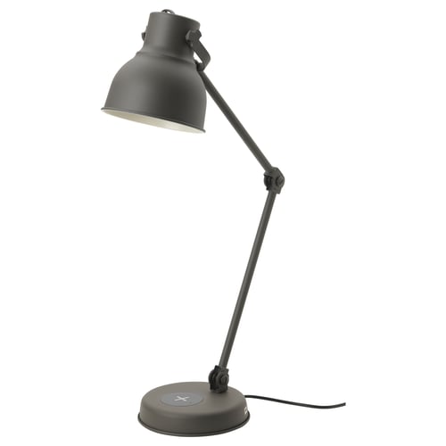 A black HEKTAR desk lamp with an adjustable metal arm, a wireless charging pad, and a usb port, offering versatile lighting and charging options.