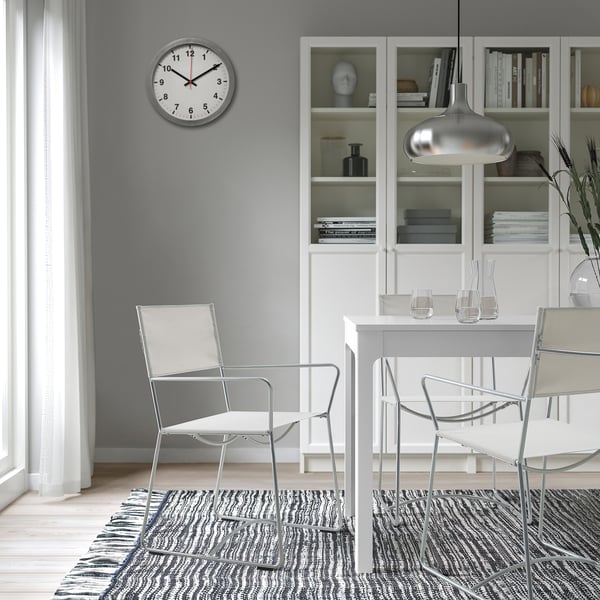 Modern dining area with HÖGALT chair, table, and clock. Wine glasses, carafe, and bookshelf in background.