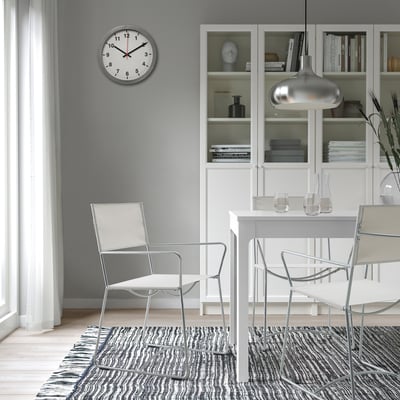 Modern dining area with HÖGALT chair, table, and clock. Wine glasses, carafe, and bookshelf in background.