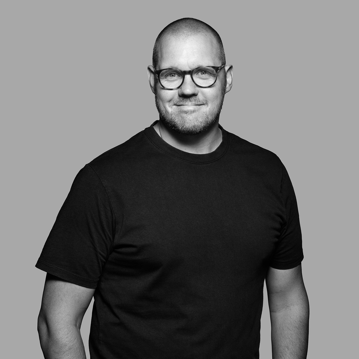Black and white photo of the designer wearing glasses and a dark t-shirt, smiling slightly.