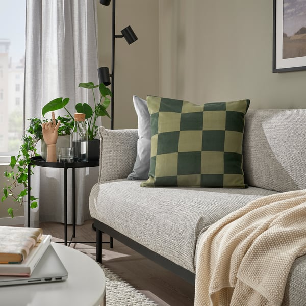 Cosy living room with grey sofa, green/black cushions, workspace table with laptop/books, black side table with plants.