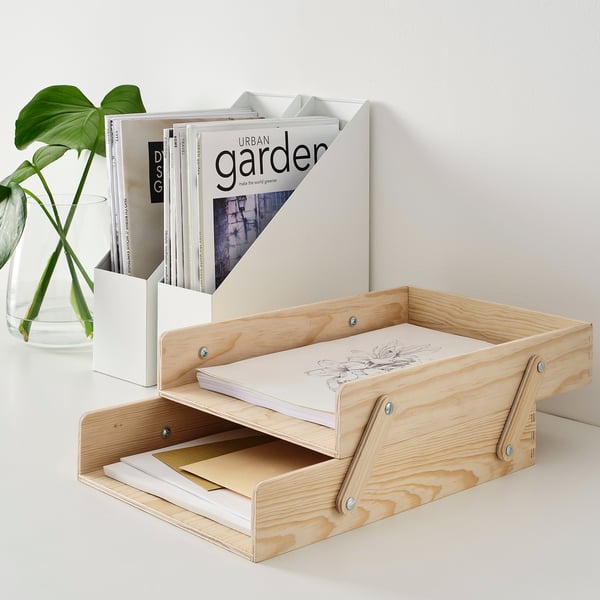 Wooden trays hold papers, next to a green plant in a glass vase.