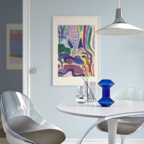 Modern dining area with clear KRYPOXBÄR chairs, small blue glass vase on white table, abstract wall art.