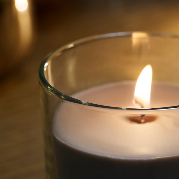 Close-up of lit scented candle; glass cup, flickering flame, warm glow.