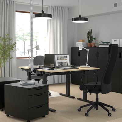 Modern black office chair with high back and armrests, positioned at sleek, black desk with grey carpet, surrounded by storage units and plants.