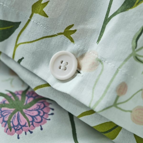 Close-up of a white button on a pale blue duvet cover with floral designs, securing a folded edge.
