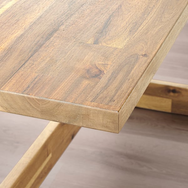 A close-up of a sturdy, acacia wooden table with smooth, polished edges and visible wood grain.