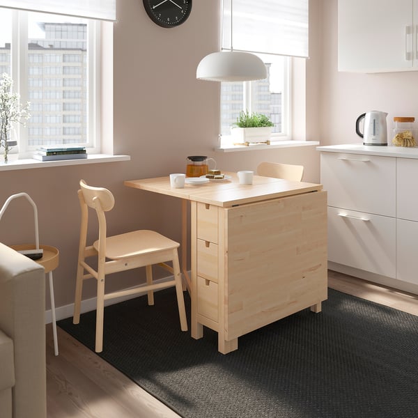 Small light wood NORDEN dining set with table, two chairs, and rug in a cosy kitchen space.