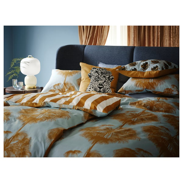 Tropical-themed bedroom with blue sofa, palm bedding, lamp, and plant.
