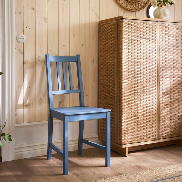 A blue PINNTORP chair with a vertical slat back made of solid pine, placed against a wooden wall and next to a woven storage unit.