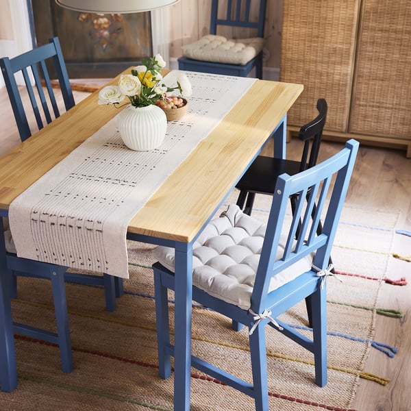 Cosy dining setup with wooden table, blue chairs, beige runner, and vase of white flowers.