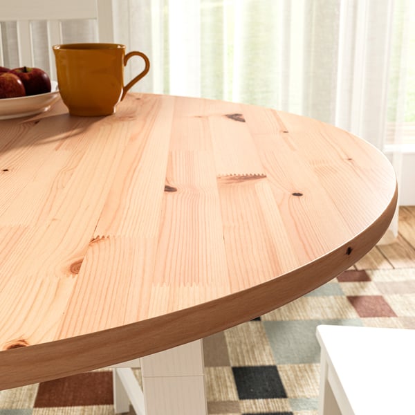 Wooden table with light finish and smooth edges, yellow mug, patterned rug, close-up.