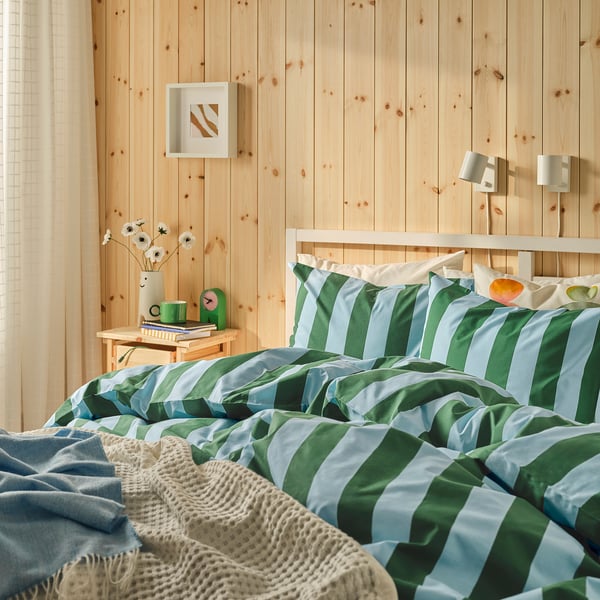 Cosy bedroom with SLÅNHÖSTMAL duvet, knitted blanket, bedside table with books, and wall lamps.