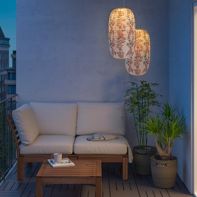 Balcony with two SOLVINDEN solar lamps above a beige sofa. Lamps are white with plant patterns, illuminating the cosy space.