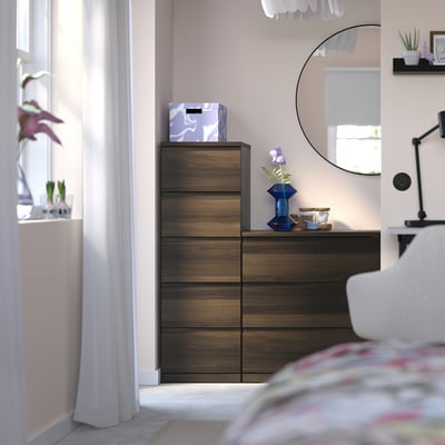 Modern wooden chest STORKLINTA with drawers by window, bed, mirror. Dark brown, pastel walls, sleek design.