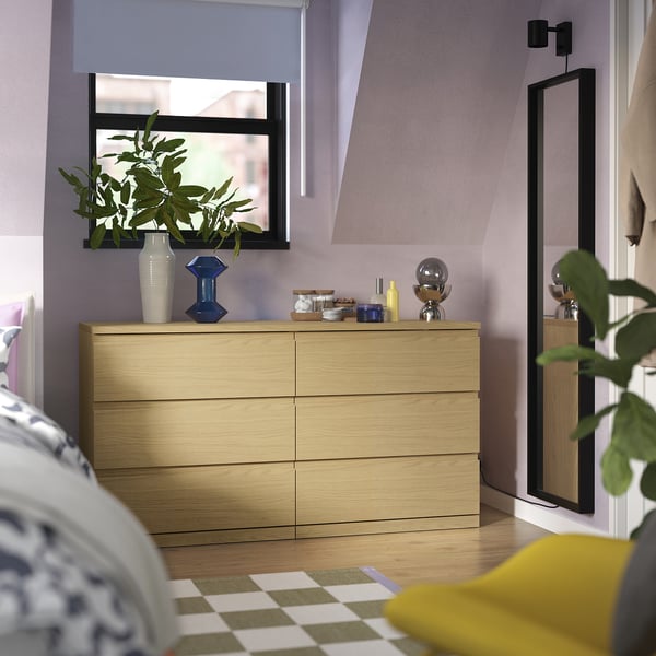 Modern 6-drawer light wood chest with vases, plant, and mirror-topped dresser.