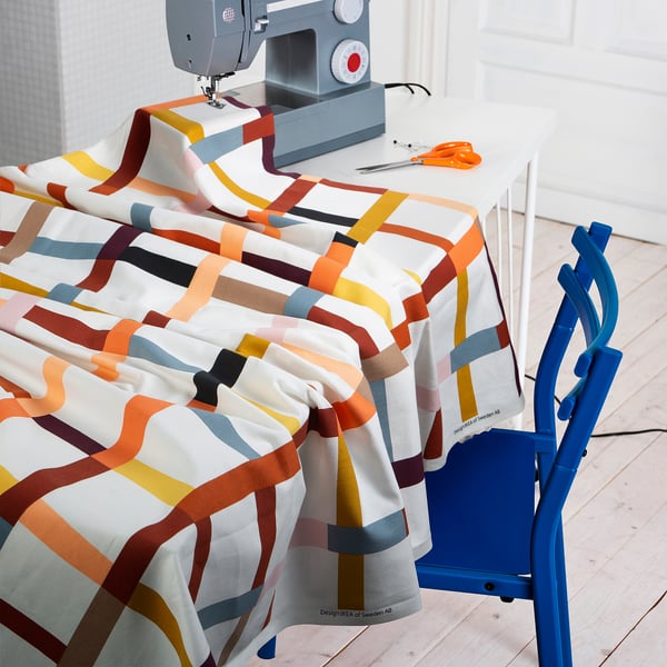 A sewing station with colourful striped fabric draped over a white table, a sewing machine, and blue chair, ready for crafting curtains or home decor.