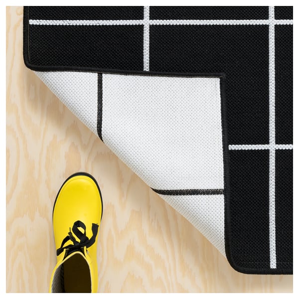 Bright yellow shoe steps on a black and white chequered indoor/outdoor rug on a wooden floor.