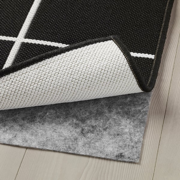 Black and white patterned rug with a soft underside, likely for non-slip use, placed on wooden flooring.