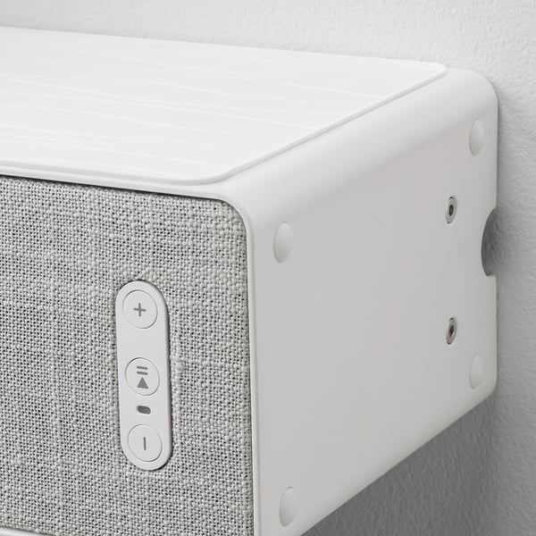 Close-up of white wall-mounted speaker with controls and screws.