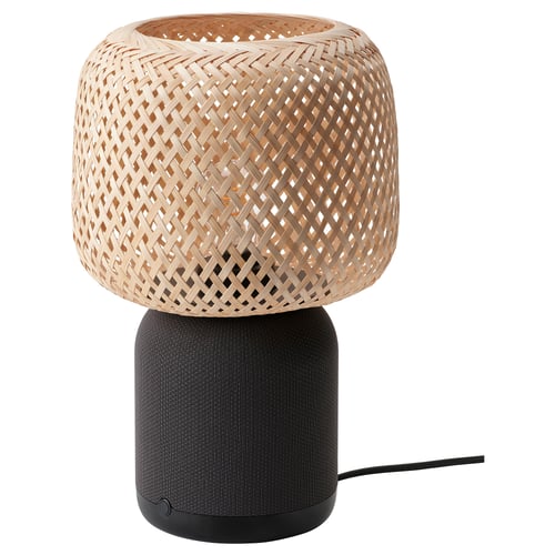 An ikea SYMFONISK table lamp with a woven bamboo lampshade atop a black fabric-covered speaker base.