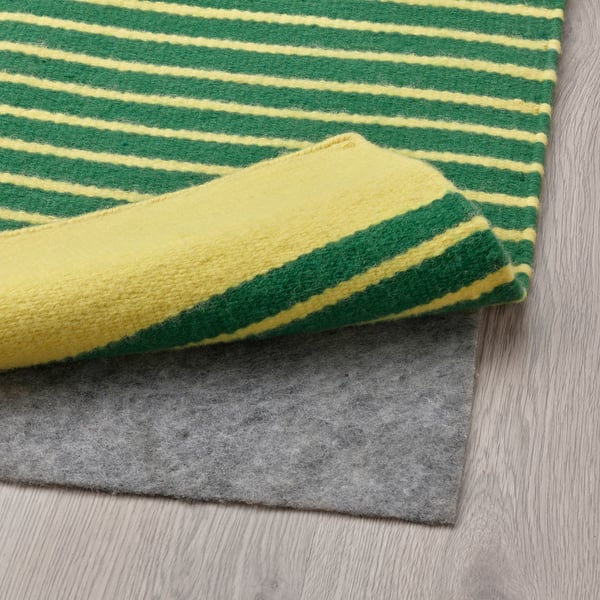 Striped green and yellow rug, folded to show non-slip pad underneath.