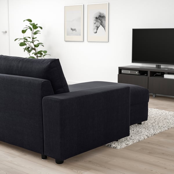 Modern living room with black VIMLE sectional sofa, ottoman, and tv stand. Minimalist decor with white walls and plant.