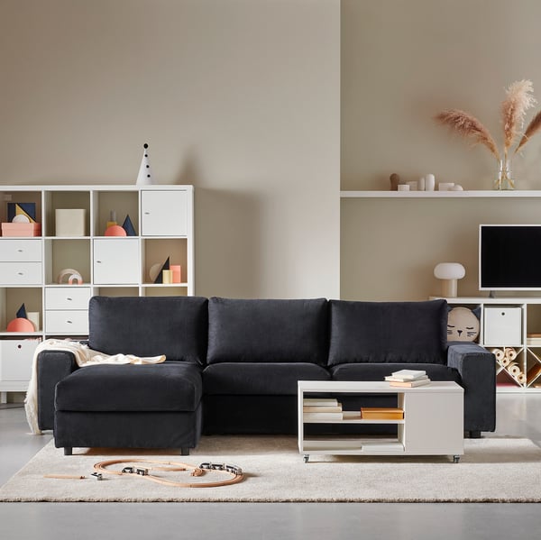 Modern living room: dark grey l-shaped VIMLE sectional sofa on beige rug, facing white storage units with colourful accents and tv.