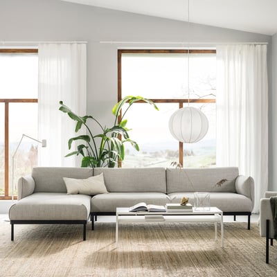 Modern living room with grey l-sofa, white coffee table, plant. Bright, big windows.