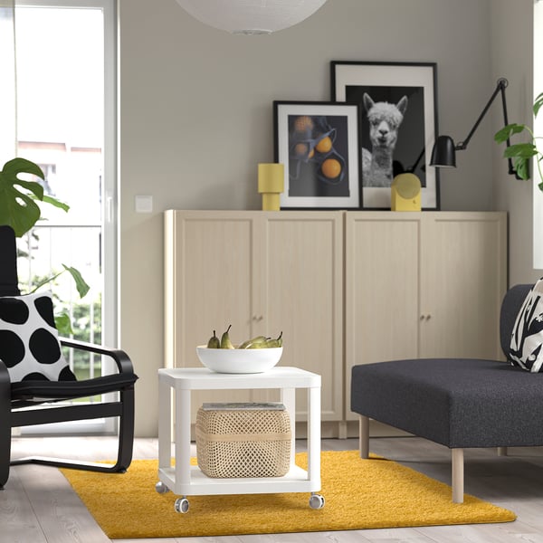 Modern living room with golden rug, light cabinet, fruit bowl table, armchair, sofa, and wall art.